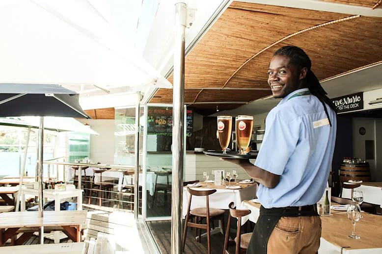 A smiling waiter carrying two draught beers
