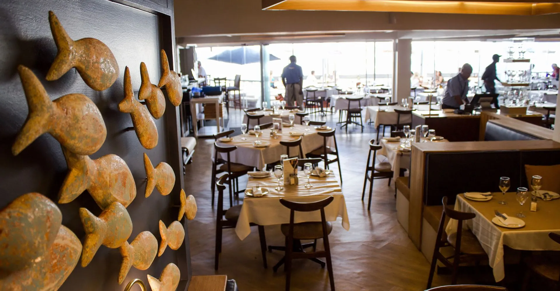 The dining room with a shoal of bronze fish on the wall and the harbour through the windows