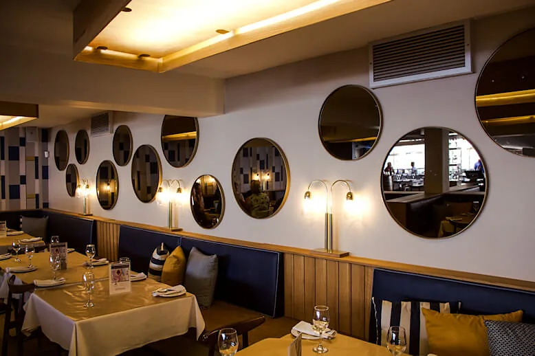 Round porthole mirrors along the dining-room wall above navy banquettes